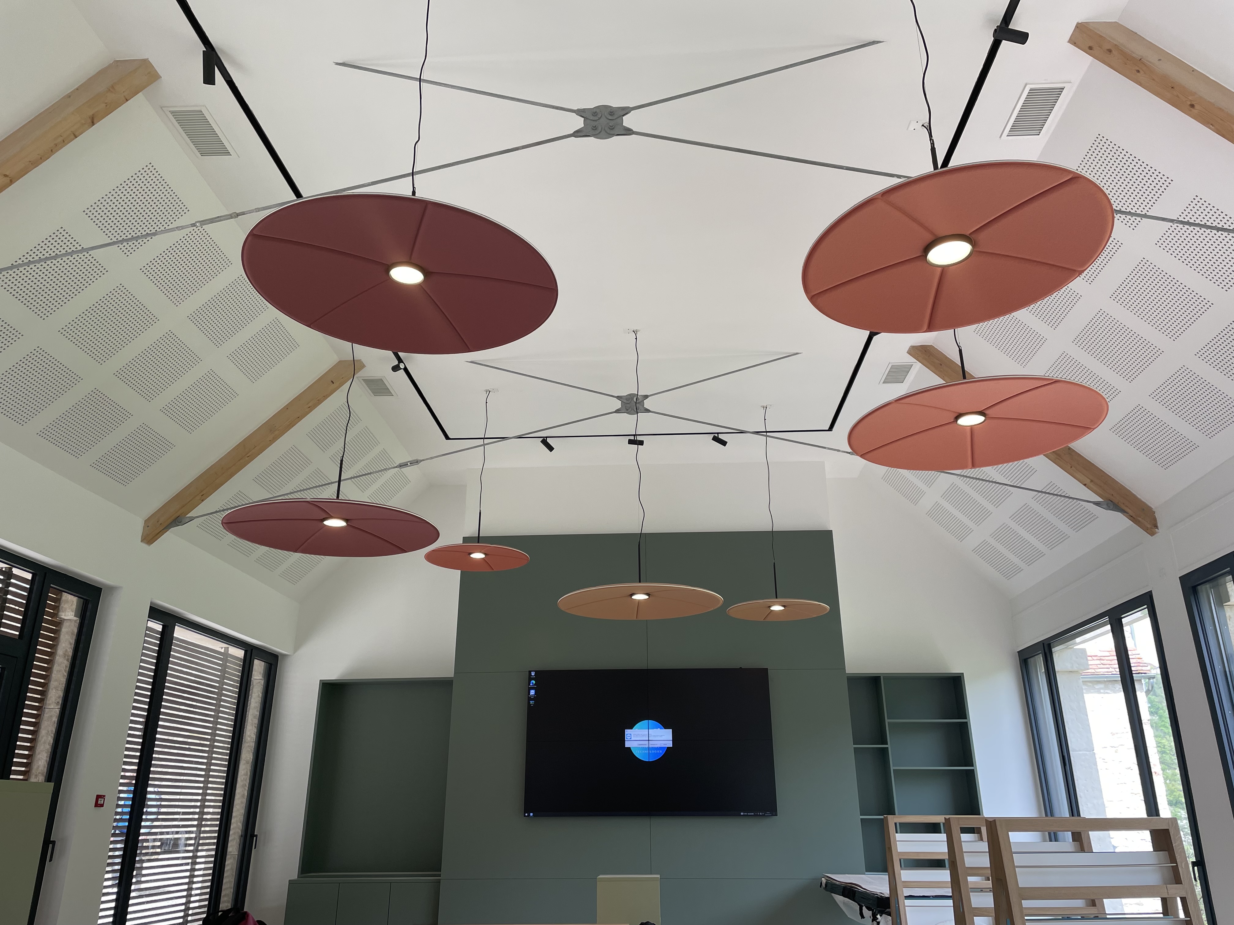 Espace d'accueil intérieur : Plafond cathédrale avec luminaires acoustiques en forme de disques colorés et comptoir d'accueil en bois clair.