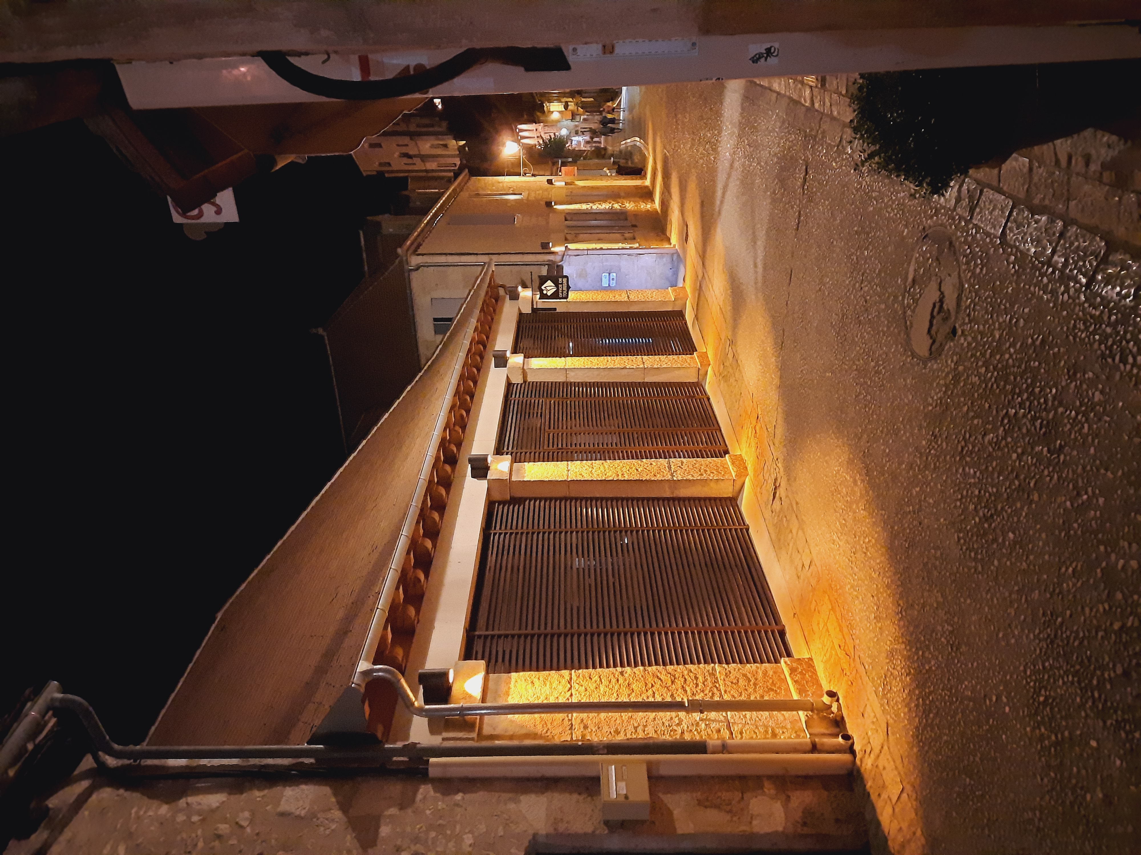 •	Façade extérieure la nuit : L'office de tourisme avec ses volets à lames horizontales et son éclairage mettant en valeur la pierre calcaire locale.