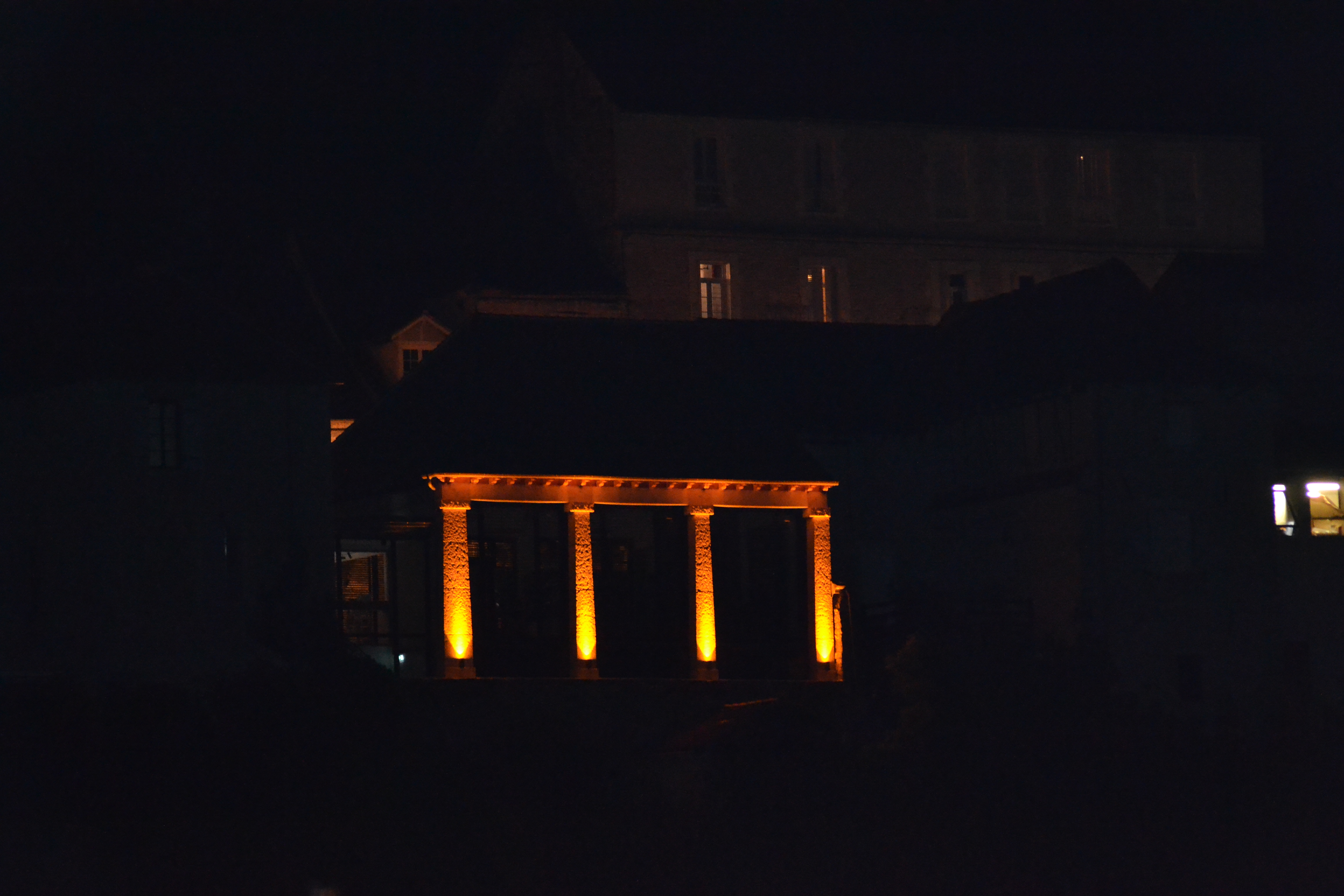 Façade extérieure la nuit : L'office de tourisme avec ses volets à lames horizontales et son éclairage mettant en valeur la pierre calcaire locale.